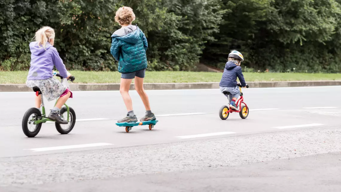 3 enfants en bas-âge sur un vélo, une draisienne et un skate